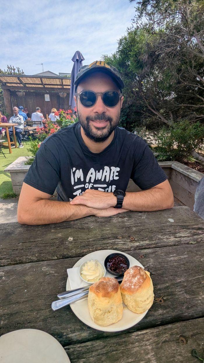 Gilad smiling at a cafe table with two scones, jam and cream