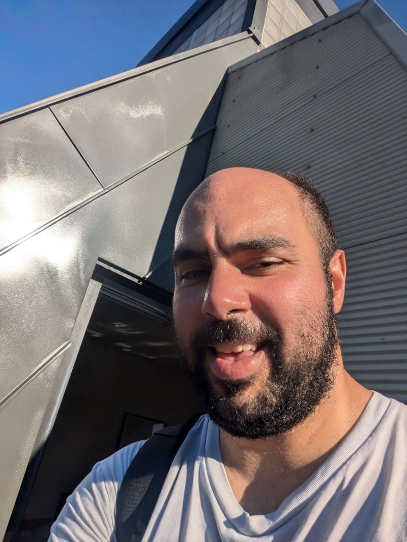 Gilad squinting in the sun in front of an angular metal-clad building